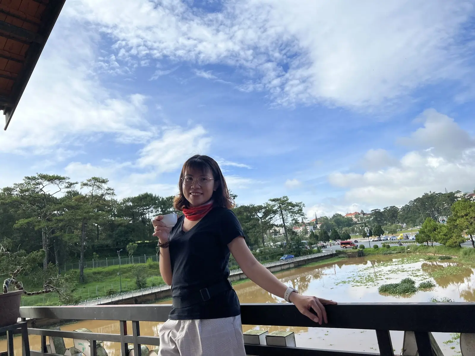 Loo cầm ly đứng bên lan can nhìn ra hồ và rừng cây